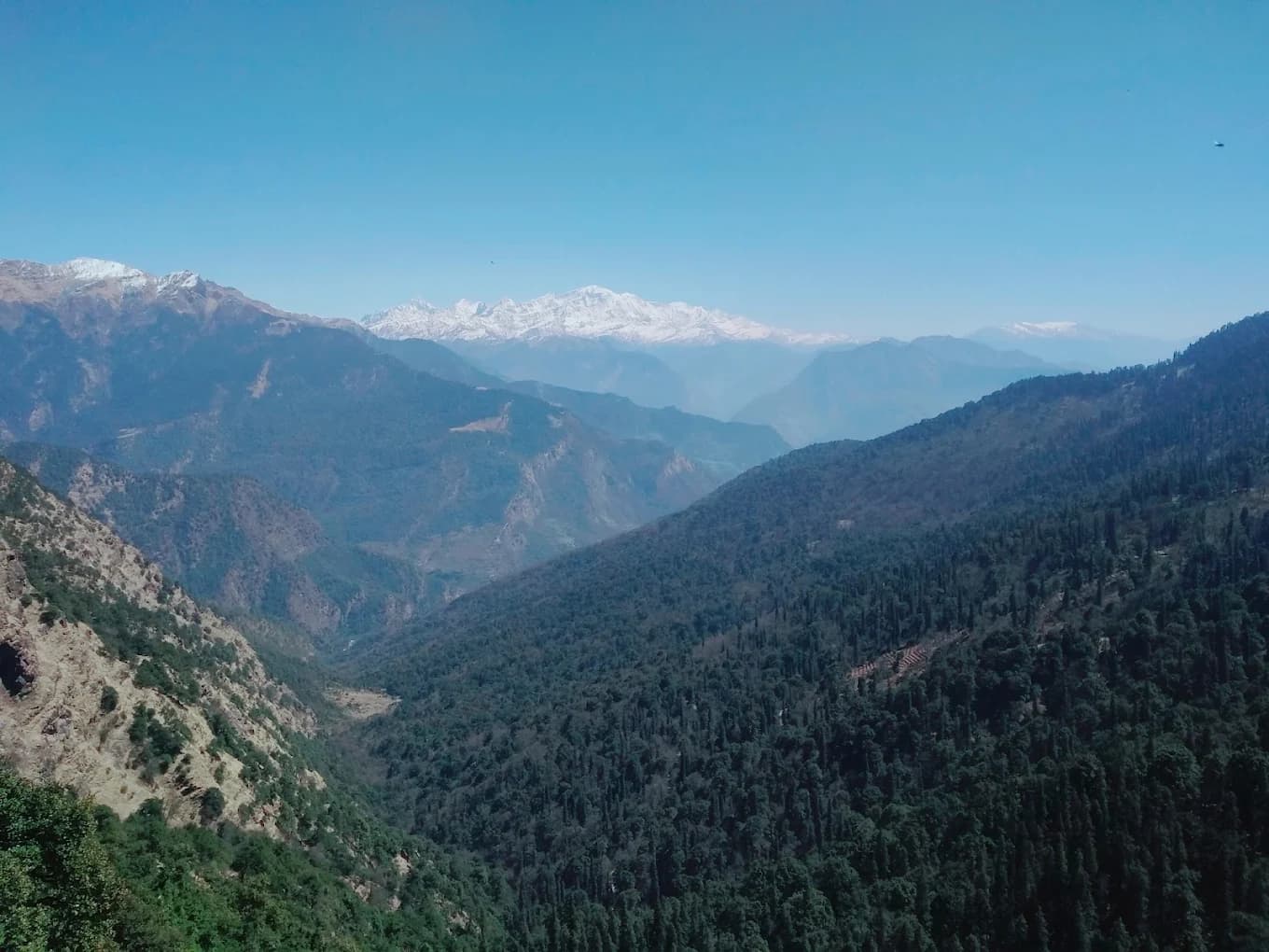 A wide Himalayan valley with layered ridges fading into haze