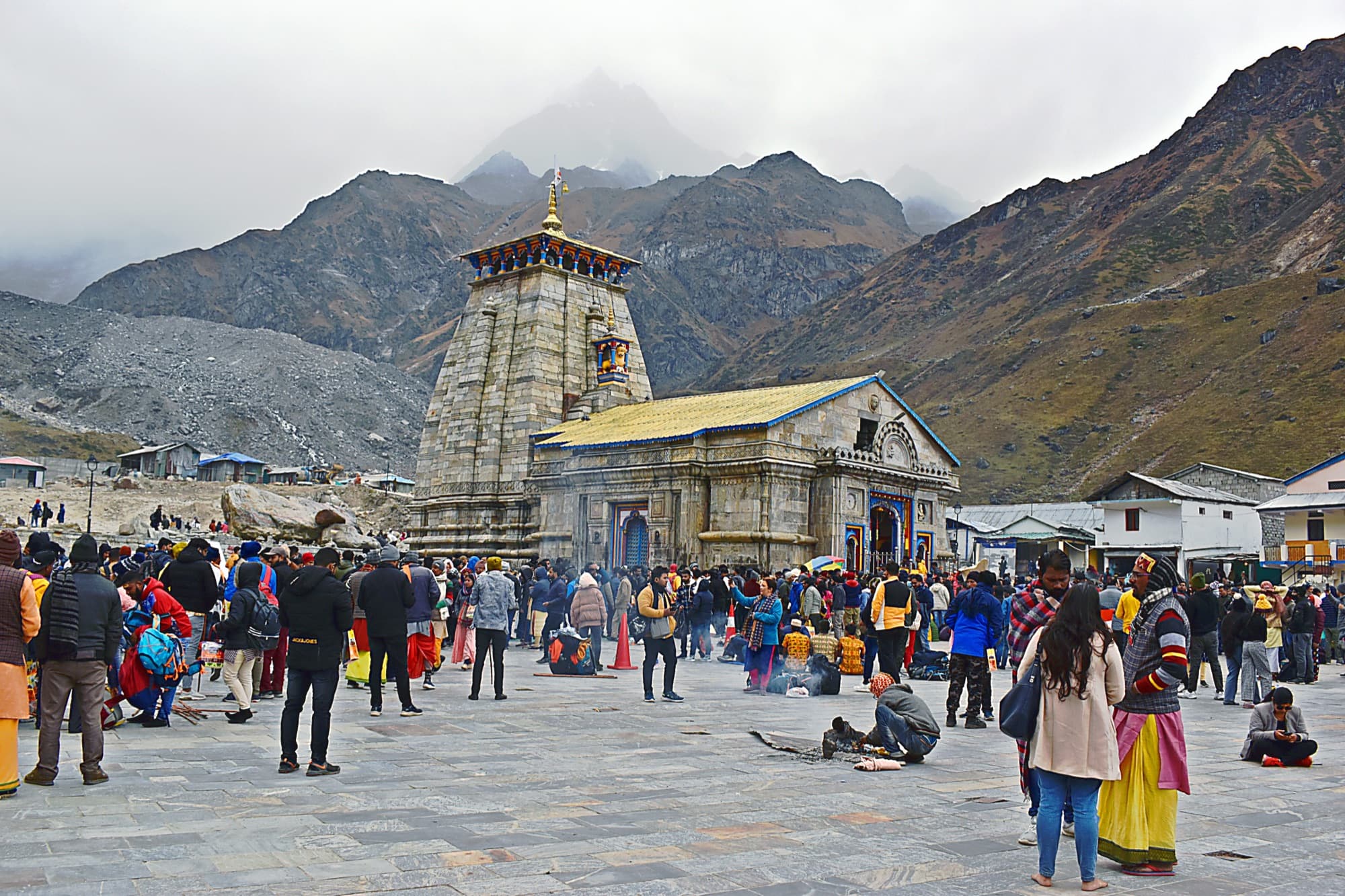 Pilgrims in the courtyard before Kedarnath temple, with low cloud on the mountains